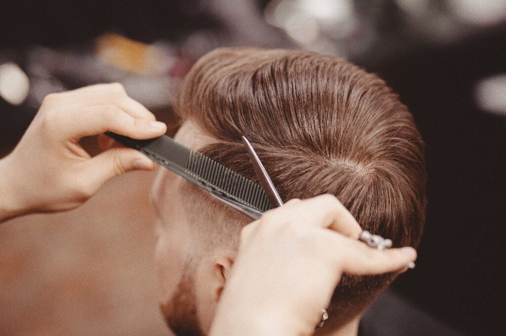 Close-up, master hairdresser does hairstyle with scissors comb. Concept Barbershop